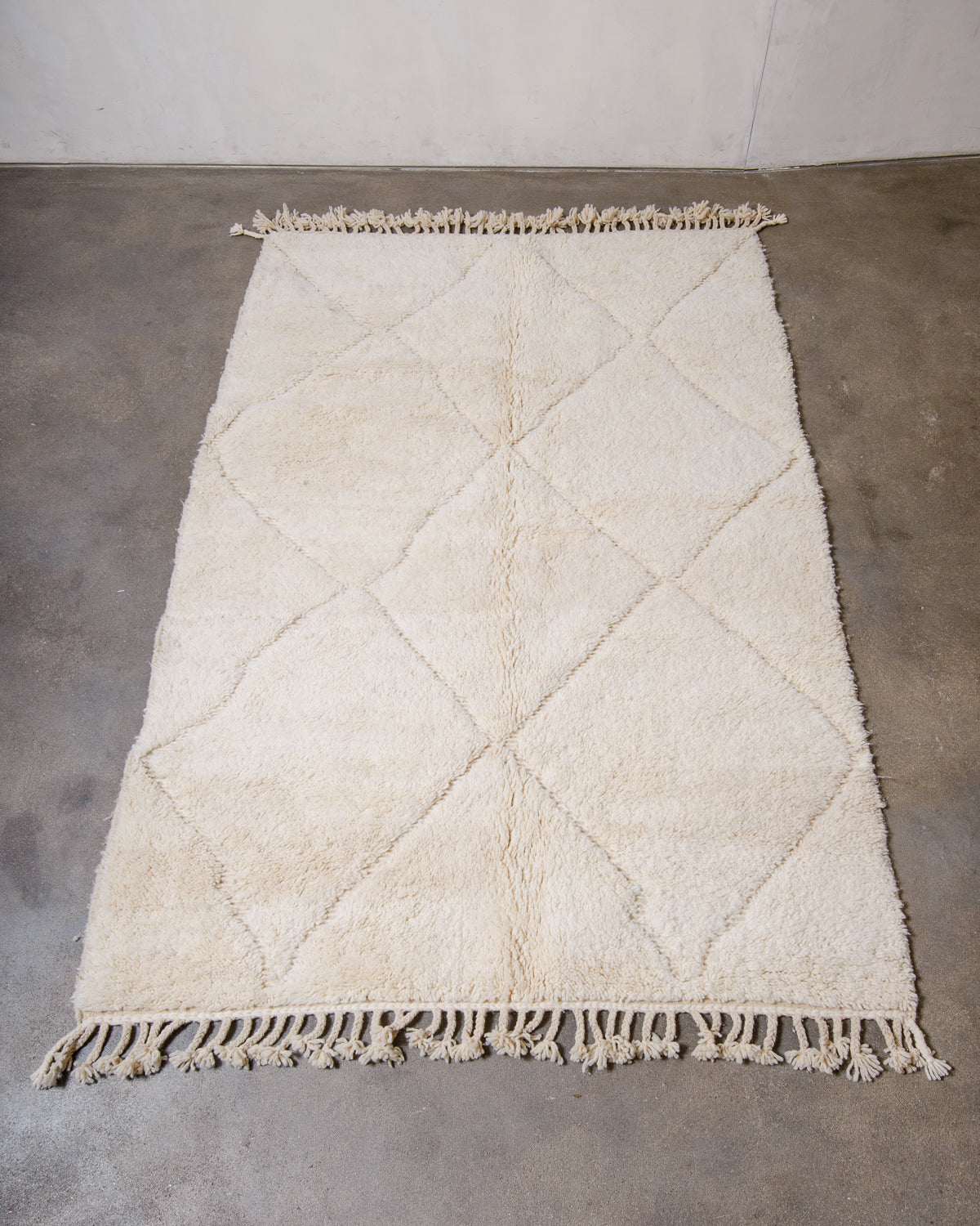 Berberlin Beniourain rug made of cream wool laying flat on concrete floor.
